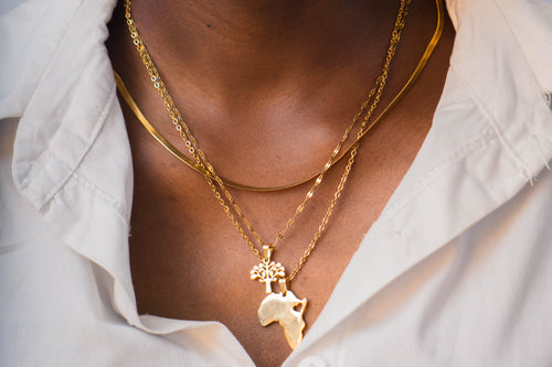Close-up of a woman wearing gold a gold african necklaces with a neutral background