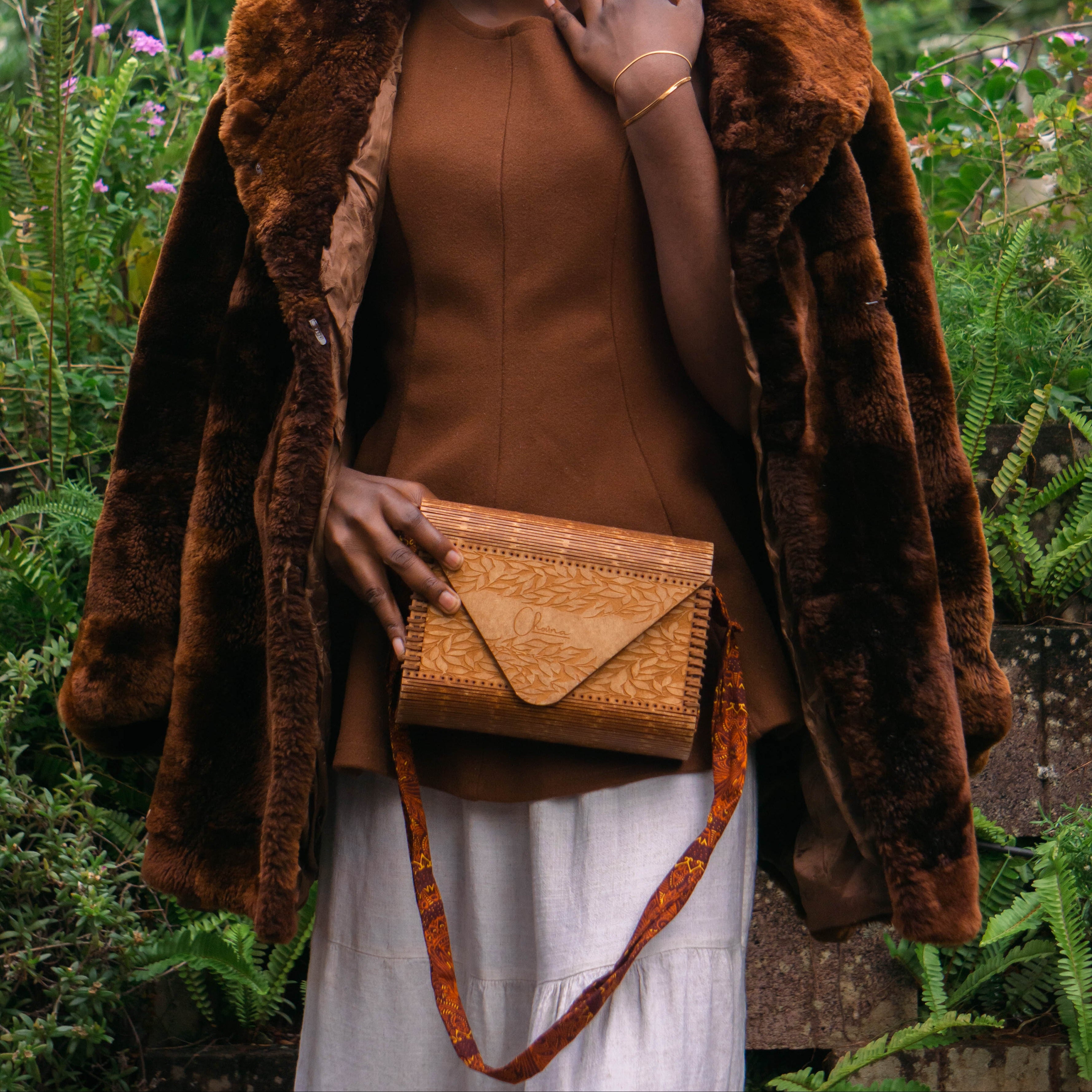 Woman holding a woven handbag in a garden setting